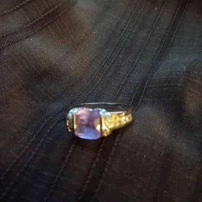 Silver-tone ring featuring a cushion-cut purple gemstone, flanked by small pave-set accent stones on the shoulders.