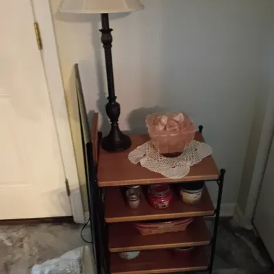 Longaberger Four-tier wood and metal shelving unit holding a salt lamp, decorative candles, a tall dark table lamp, and various home...