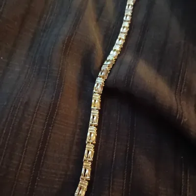 Gold-tone tennis bracelet featuring articulate bar-style links and a secure fold-over clasp, displayed against dark fabric.