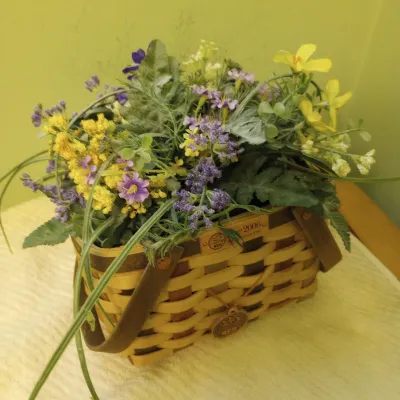 Sale Photo Thumbnail #11: A 2006 Longaberger woven basket filled with an arrangement of colorful artificial wildflowers and greenery.