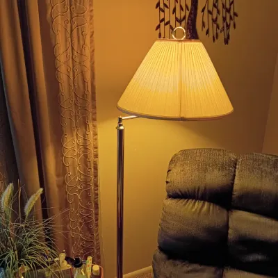Sale Photo Thumbnail #58: Traditional brass swing-arm floor lamp with a pleated fabric shade, shown illuminated beside a upholstered recliner.