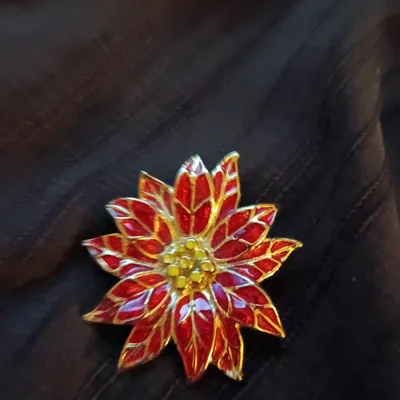 Gold-tone poinsettia brooch featuring vibrant red enamel petals and yellow enamel accents at the center.