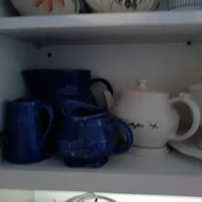 Sale Photo Thumbnail #68: Collection of vintage ceramic teapots, pitcherset, and creamers stored on white shelving, featuring floral motifs and cobalt blue glazes.