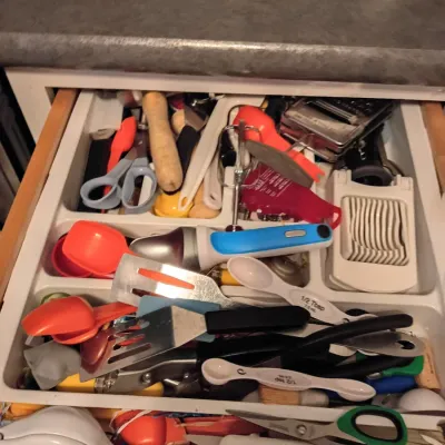 Sale Photo Thumbnail #37: Open kitchen drawer filled with an assortment of utensils, including spatulas, measuring spoons, scissors, an egg slicer, and a hand mixer attachment.
