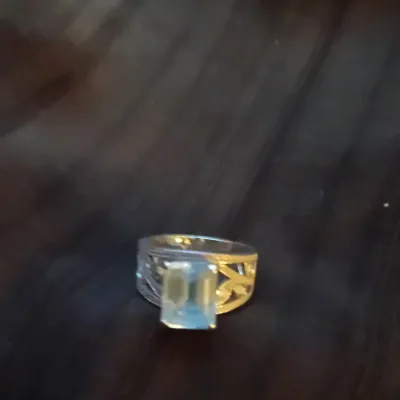 Silver-tone ring featuring a large emerald-cut light blue or clear gemstone with ornate, filigree-style band detailing.