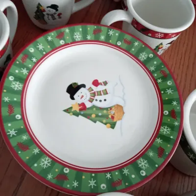 Sale Photo Thumbnail #16: Holiday ceramic tableware featuring snowman motifs, including dessert plates and matching coffee mugs.
