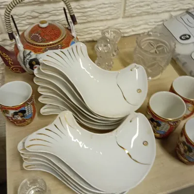 Sale Photo Thumbnail #28: Set of white porcelain fish-shaped plates with gold accents, displayed alongside an Asian teapot set and small glassware.