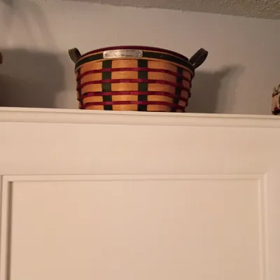 Sale Photo Thumbnail #46: Longaberger woven basket featuring red and green accent weaving, leather handles, and a commemorative metal plaque, sitting atop a white cabinet.