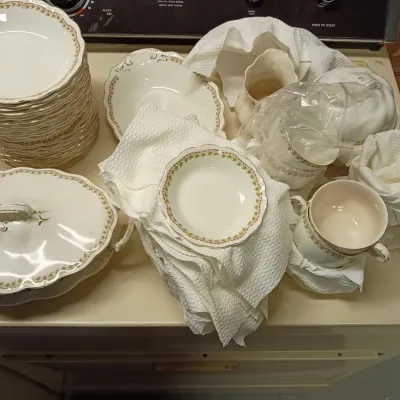 Sale Photo Thumbnail #22: Vintage white porcelain dinnerware set with delicate floral border trim, including a stack of plates, serving dishes, teacups, and a covered tureen, packed with paper padding.