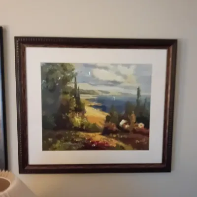 Sale Photo Thumbnail #62: Framed impressionistic coastal landscape painting featuring cypress trees and rolling hills overlooking a blue sea, housed in a dark wooden frame with a white mat.