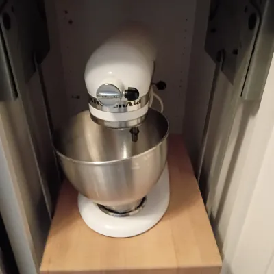 Sale Photo Thumbnail #43: White KitchenAid stand mixer with stainless steel mixing bowl, resting on a wooden pop-up cabinet shelf mechanism.