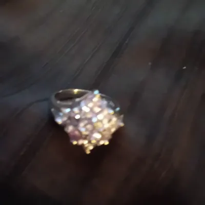 Silver-tone cluster ring set with multi-colored faceted gemstones resting on a dark wood surface.