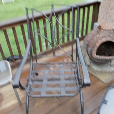 Sale Photo Thumbnail #39: Black wrought iron outdoor armchair with a geometric openwork backrest, positioned on a wooden deck next to a terracotta chiminea.
