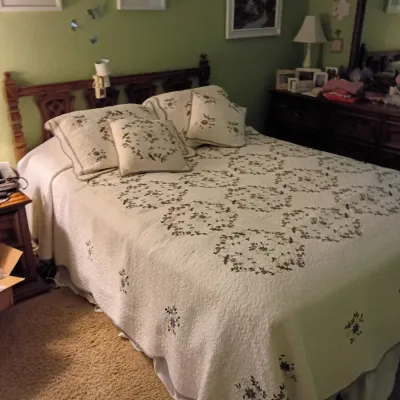 Sale Photo Thumbnail #50: Traditional full-sized bed frame with an carved wooden headboard, featuring a cream-colored embroidered floral quilt with matching shams and throw pillows.