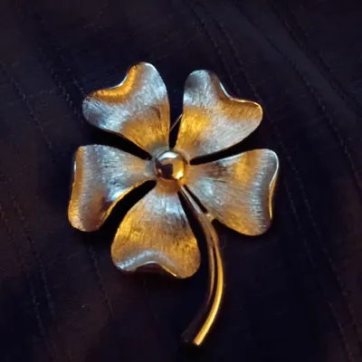 Vintage gold-tone four-leaf clover brooch featuring a textured, brushed finish on the leaves and a smooth polished center and stem.