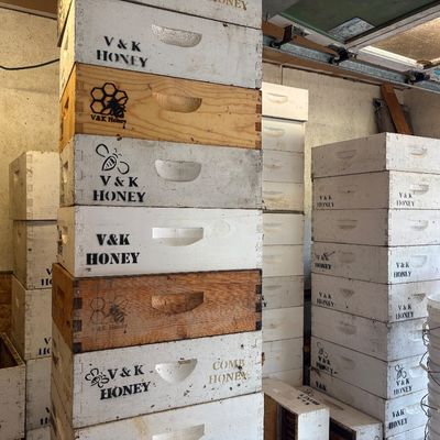 Sale Photo Thumbnail #55: Stacks of wooden beekeeping supers and hive boxes branded with "V&K Honey," showing various states of wear and paint finishes.