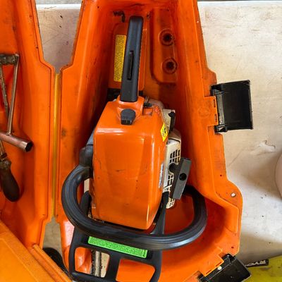Sale Photo Thumbnail #30: Stihl gas-powered chainsaw resting inside an orange plastic hard-shell carrying case.