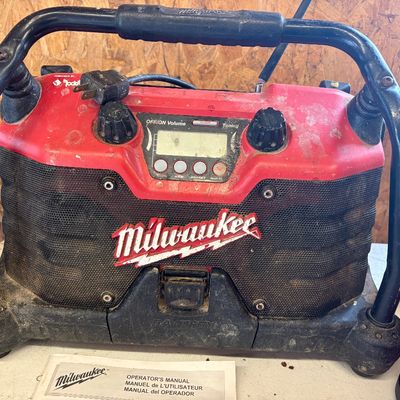 Sale Photo Thumbnail #33: Milwaukee jobsite radio featuring a heavy-duty protective cage, digital tuner, and attached power cord, showing heavy wear from use and paired with its original operator's manual.