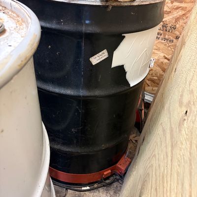 Sale Photo Thumbnail #57: Large black metal drum with a red base heater, showing some wear and labeling, stored alongside other containers.