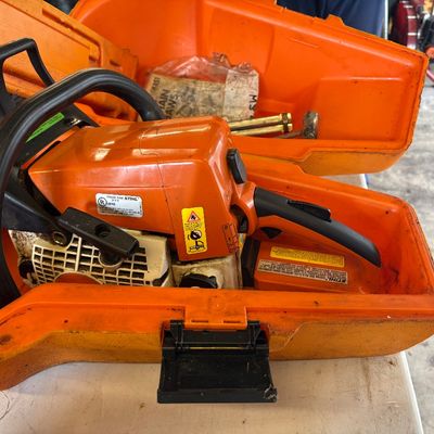Sale Photo Thumbnail #29: Stihl gas-powered chainsaw resting inside its original orange hard plastic carrying case.