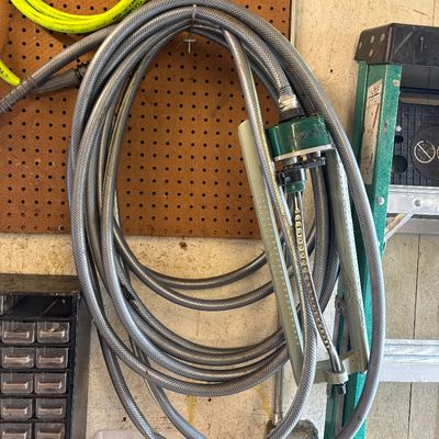 Sale Photo Thumbnail #10: Coiled grey garden hose hanging on a pegboard, featuring an attached Orbit oscillating lawn sprinkler attachment.