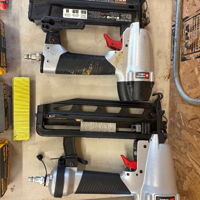 Sale Photo Thumbnail #23: Two Porter-Cable pneumatic nail guns alongside boxes and strips of nails on a work table.
