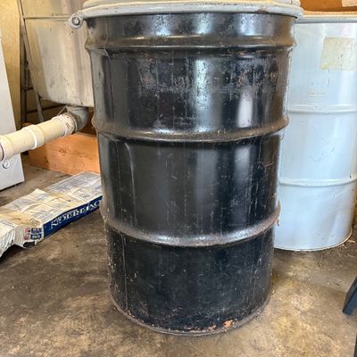 Sale Photo Thumbnail #59: Vintage 55-gallon black metal drum container with a clamp-style lid, showing minor surface wear and light rust along the edges.