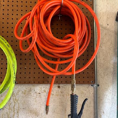 Sale Photo Thumbnail #20: Coiled bright orange air hose with a blow gun attachment hanging from a pegboard hook.
