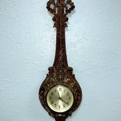 Sale Photo Thumbnail #390: Vintage New Haven Clock Co. 8-day banjo-style wall clock featuring a heavily carved ornate dark wood frame.