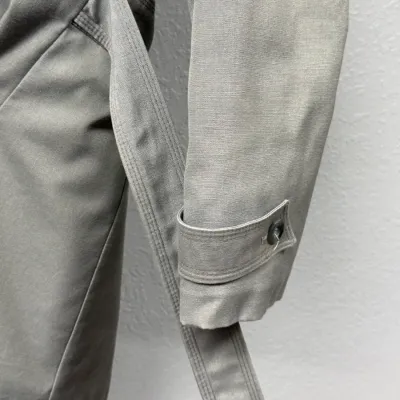 Sale Photo Thumbnail #869: Close-up detail of a vintage olive green trench coat sleeve featuring a buttoned cuff strap and matching fabric waist belt.
