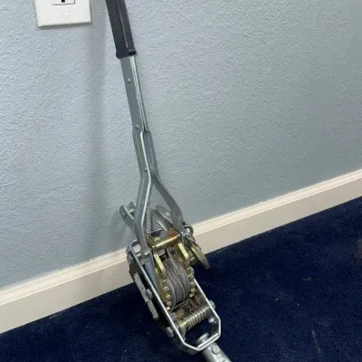 Sale Photo Thumbnail #658: Heavy-duty ratchet puller hand winch with steel cable and attached hook, showing light cosmetic wear.