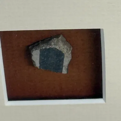 Sale Photo Thumbnail #487: Framed geological specimen or mineral sample mounted on a brown background within a white matting frame.