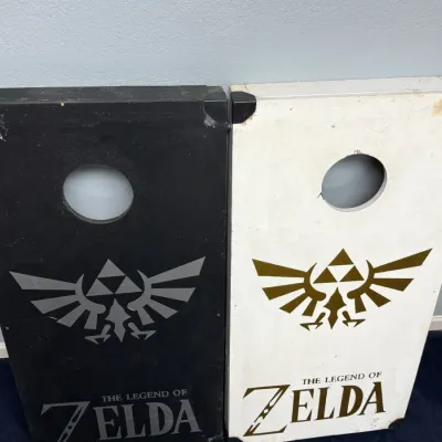 Sale Photo Thumbnail #923: Pair of custom Legend of Zelda-themed cornhole boards in contrasting black and white finishes, showing surface scuffs and wear.