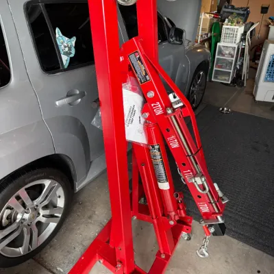 Sale Photo Thumbnail #513: Foldable red 2-ton hydraulic shop crane engine hoist, stored upright in a garage.