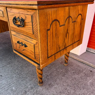 Sale Photo Thumbnail #258: Vintage oak desk featuring twisted rope legs, dark metal hardware, and decorative molded paneling along the side.