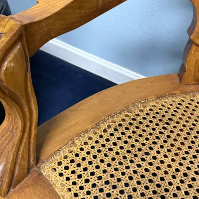 Sale Photo Thumbnail #674: Close-up of a vintage wooden armchair featuring a carved frame, contoured armrest, and a woven cane seat.