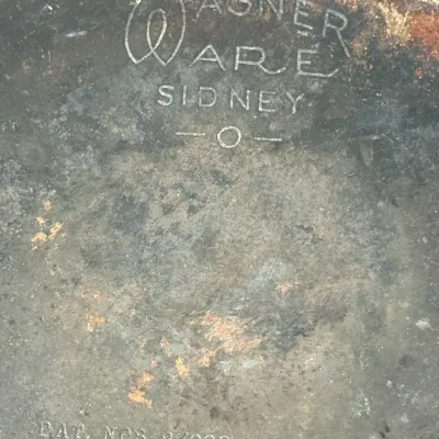 Sale Photo Thumbnail #585: Vintage Wagner Ware Sidney -O- cast iron or cookware base, featuring stamped logo and patent numbers with visible surface wear and oxidation.