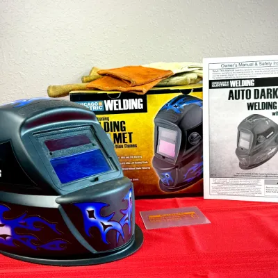Sale Photo Thumbnail #516: Chicago Electric auto-darkening welding helmet with blue flame graphics, complete with original box, owner's manual, and welding gloves.