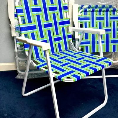 Sale Photo Thumbnail #916: Vintage-style folding lawn chair featuring blue and green woven webbing on a white aluminum frame. Additional matching folded chairs sit in the background.