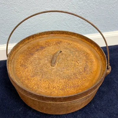 Sale Photo Thumbnail #593: Vintage cast iron Dutch oven with lid and wire bail handle, showing heavy surface rust.
