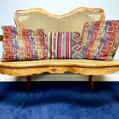 Sale Photo Thumbnail #670: French Provincial style carved wood and cane settee, featuring cabriole legs and ornate curved arms, accompanied by three patterned throw pillows.