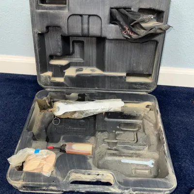 Sale Photo Thumbnail #626: Dusty black molded plastic tool carrying case with various accessories, including wrenches, oil, wooden biscuits, and a fabric pouch, missing the primary power tool.