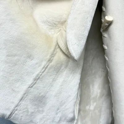 Sale Photo Thumbnail #850: Close-up interior view of a cream-colored shearling coat, showing the soft plush lining, stitched seams, and toggle button closures.