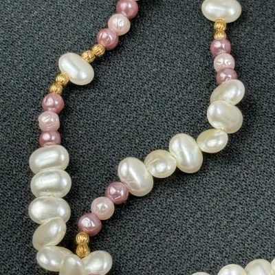 Sale Photo Thumbnail #191: Strand of freshwater pearls featuring alternating iridescent white and dusty rose pearls interspersed with small gold-toned spacer beads.