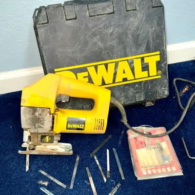 Sale Photo Thumbnail #600: DeWalt corded jigsaw with hard carrying case and a collection of assorted blades, showing light wear from use.