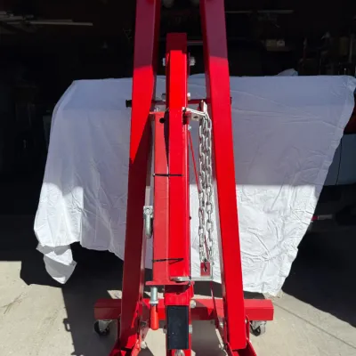 Sale Photo Thumbnail #506: Red foldable hydraulic engine hoist crane on casters, shown folded for storage in a driveway.