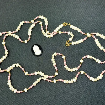 Sale Photo Thumbnail #190: Long freshwater pearl strand necklace with pink accent beads, gold-tone clasps, and an oval cameo cabochon.