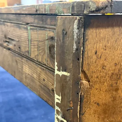 Sale Photo Thumbnail #286: Close-up detail of a rustic antique wooden workbench showing heavy wear, paint remnants, and aged joinery.