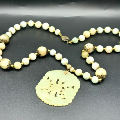 Sale Photo Thumbnail #357: Vintage Asian carved celadon jade pendant necklace featuring hand-carved openwork central plaque and decorative brass-capped jade bead strand.