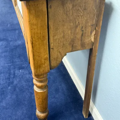 Sale Photo Thumbnail #282: Side profile of a vintage or antique wooden counter table showing turned front legs and heavy wear on the tabletop finish.
